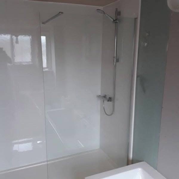 White wall-panelled shower with a glass screen and riser rail